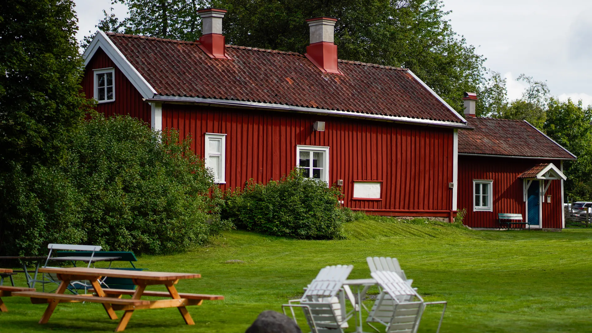 Rødt trehus med velholdt plen og hagemøbler i grønne omgivelser
